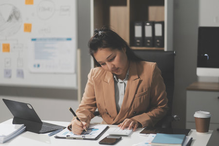Asian Businesswoman Using laptop computer and working at office with calculator document on desk, doing planning analyzing the financial report, business plan investment, finance analysis concept.の写真素材