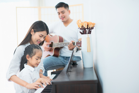 Asian family, Mother and daughter playing piano,Father playing guitar in family band at home, Concept for family relationshipの写真素材