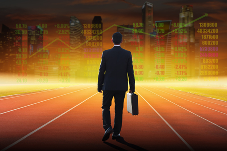 Businessman on a track ready for race in business on blurred city background.の写真素材