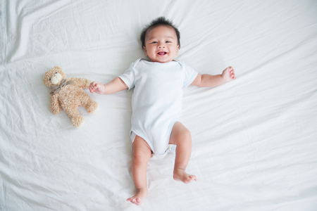 Portrait of a crawling baby on the bed in her room, Adorable baby boy in white sunny bedroom, Newborn child relaxing in bed, Nursery for young children, Textile and bedding for kidsの写真素材