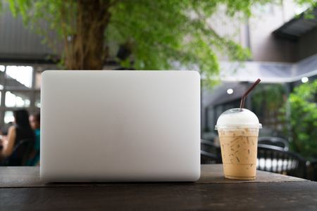 Laptop and coffee cup on wooden table, Laptop with blank screen on table. coffee shop blurred background. Business concept.の写真素材