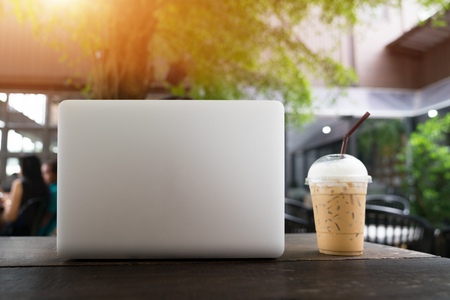 Laptop and coffee cup on wooden table, Laptop with blank screen on table. coffee shop blurred background. Business concept.の写真素材