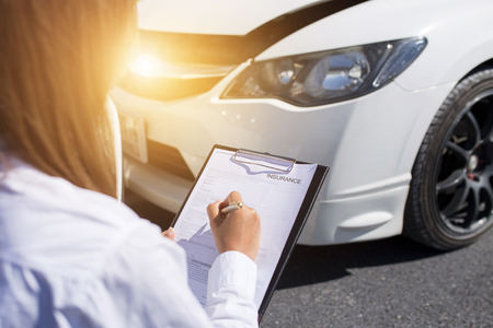 Side view of writing on clipboard while insurance agent examining car after accidentの写真素材