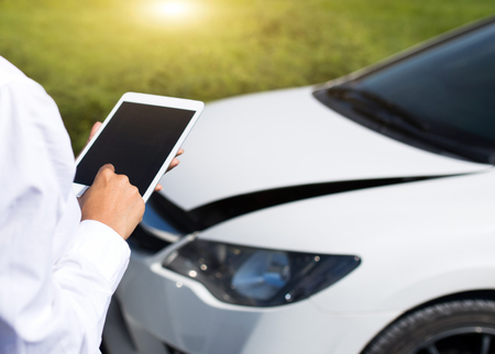Insurance agent inspecting damaged car with insurance claim form on digital tabletの写真素材
