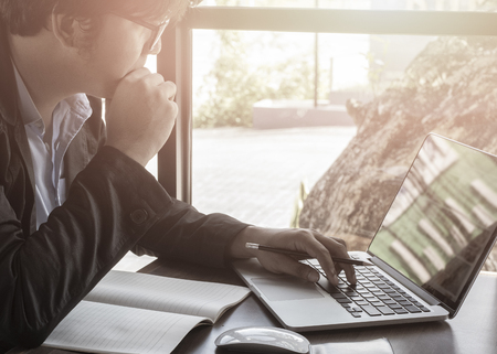 Young finance market analyst in eyeglasses working at sunny office on laptop while sitting at wooden table, Businessman analyze document in his hands, Graphs and diagramm on notebook screenの写真素材