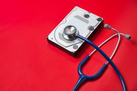 Stethoscope and hard disk drive on red background. Computer hardware diagnostic and repair concept