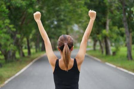 Successful woman raising arms after cross track running on summer sunset. Fitness female athlete with arms up celebrating success and goals after sport exercising and working out.の写真素材