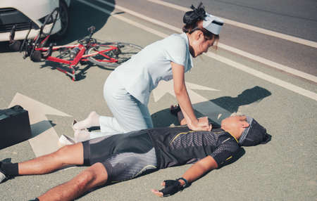 Female nurse helping emergency CPR to asia cyclist injured on the street bike after collision accident car and bikeの写真素材