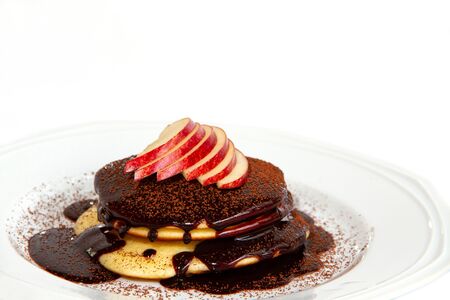 Chocolate pancake sprinkled with chocolate powder, with apples on top of a white plateの写真素材