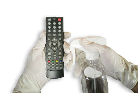 Close up. White gloved hand holding a TV remote and alcohol spray. Cleaning to prevent germs and...