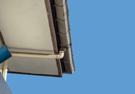 Low angle view, hip roof corner with white gutter, of a residence, on a cloudless day (blue).