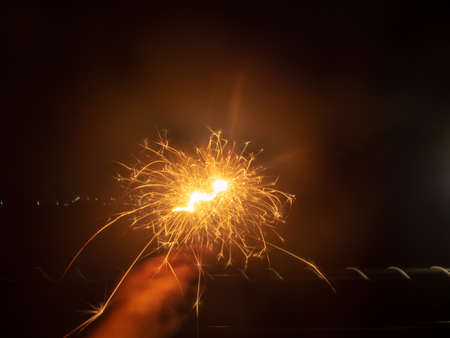 Eye-level shot, close-up. The lights and sparks of fireworks and human hands (moving) at night.の写真素材