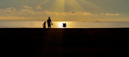 the silhouette of the seashore at sunset on vacation Nature, peace, environment and golden sunlight shines down. Chairs and lifestyle of young people in the center of the picture.の写真素材