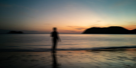 Sunrise beach and black silhouette people motion blur. Nature background sea, golden evening sky and blurred island.の写真素材