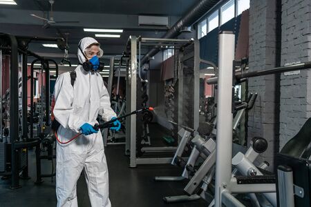professional disinfector personal protective equipment ppe suit, gloves, mask, cleaning gym space with pressurized spray disinfectant water to remove covid-19 coronavirusの写真素材
