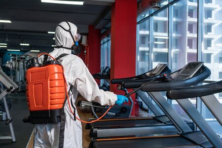 Cleaning and Disinfection in crowded places amid the coronavirus epidemic Gym cleaning and disinfection Infection prevention and control of epidemic. Protective suit and mask and spray bagの写真素材