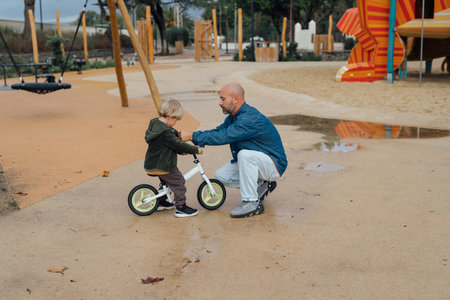 Dad teaches his son riding on bicycle in park. Father and son smile and have fun togetherの写真素材