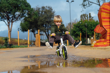 cheerful child rides a bicycle through puddles in the park. Happy childhood.の写真素材