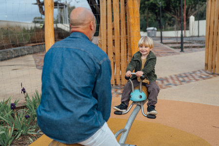 Father swinging his smiling little baby boy in a playground. Happy family.の写真素材