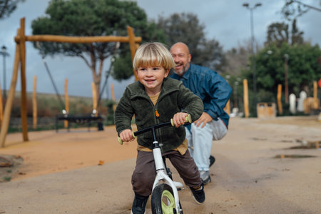 Dad teaches his son riding on bicycle in park. Father and son smile and have fun togetherの写真素材
