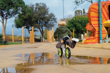 cheerful child rides a bicycle through puddles in the park. Happy childhood.の写真素材