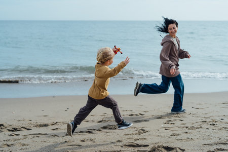 Happy mother running along the beach with her son, enjoying by the seaの写真素材