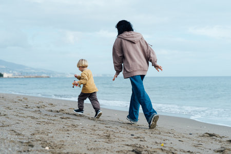 Happy mother running along the beach with her son, enjoying by the seaの写真素材