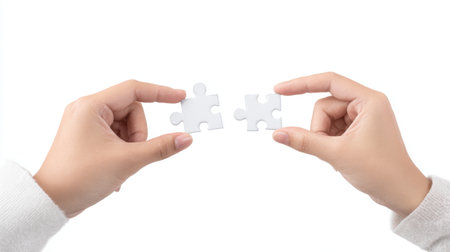 Two hands are holding individual white puzzle pieces against a clean background, representing the ideas of connection, collaboration, and team effort in solving challenges.の素材