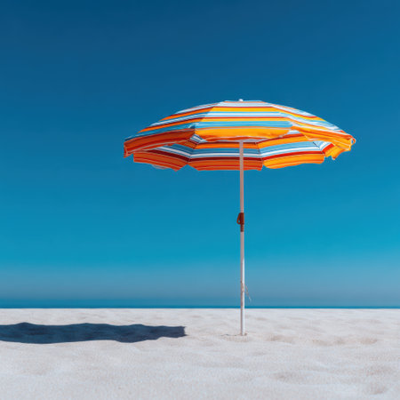 A colorful beach umbrella stands on soft white sand, providing shade against a clear sky. This image captures the essence of summer relaxation and coastal beauty, ideal for vacation memories.の素材