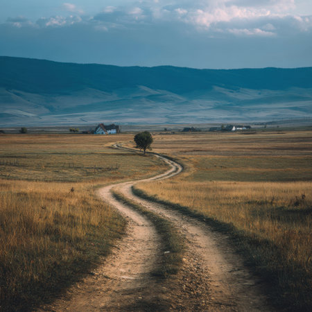 A tranquil landscape featuring a winding dirt road leading through rolling hills, flanked by an isolated tree and a distant house, under a dramatic sky. Perfect for capturing the beauty of nature.の素材