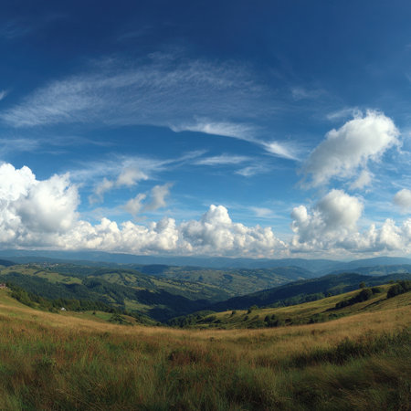A breathtaking view of green mountains under a vast blue sky adorned with fluffy white clouds. Ideal for landscape enthusiasts and nature lovers seeking serene beauty.の素材