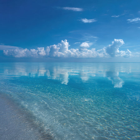 A stunning coastal view showcasing crystal clear water reflecting fluffy white clouds under a bright blue sky, evoking a sense of peace and tranquility in an idyllic setting.の素材