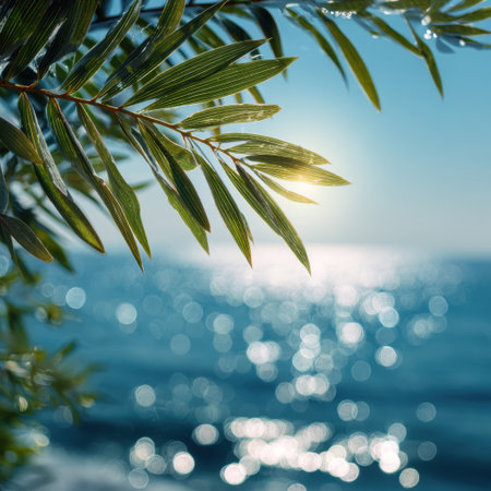 A close-up view of vibrant green leaves gently illuminated by sunlight, contrasting with the sparkling blue water in the background, evoking a tranquil and serene atmosphere.の素材