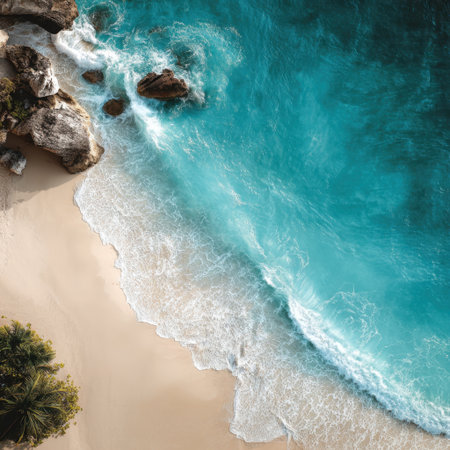 Experience the beauty of this serene aerial view showcasing turquoise ocean waves gently lapping against a sandy beach with vibrant rock formations in a sunlit coastal landscape.の素材