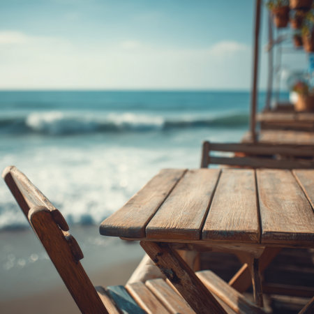 A picturesque beachfront scene showcasing a wooden table and chairs, inviting relaxation while enjoying the stunning ocean view and gentle waves under a bright blue sky.の素材