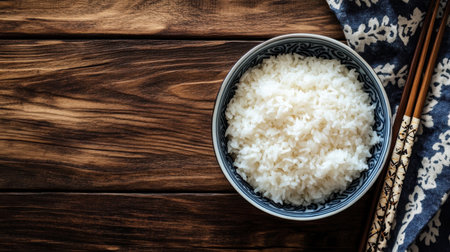 A beautifully styled image of freshly cooked white rice in a decorative bowl, placed on a wooden surface, with chopsticks ready for enjoying a simple yet elegant meal.の素材