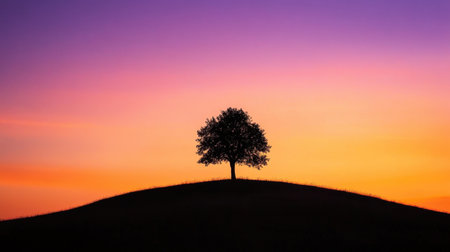 A stunning sunset scene features a lone tree silhouette atop a gentle hill, with a vibrant sky showcasing beautiful shades of purple, orange, and blue, evoking peace and serenity.の素材