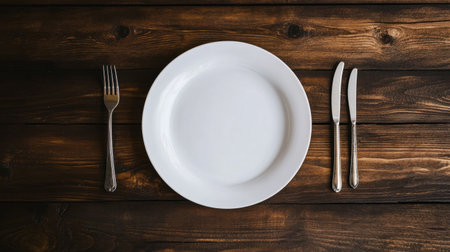 An empty white plate is gracefully placed on a rustic wooden table surrounded by silverware, perfect for showcasing dining concepts and minimalist kitchen aesthetics.の素材
