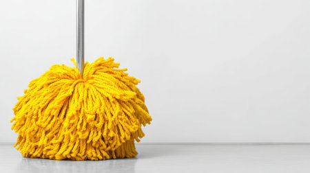 A vibrant yellow mop with fluffy strands rests on a clean floor, symbolizing effective cleaning and maintenance for homes and offices. Ideal for keeping spaces tidy and fresh.の素材