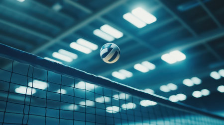 A dynamic shot of a volleyball soaring above a net in a gymnasium, highlighting the excitement and energy of indoor sports with soft lighting and a blurred background.の素材