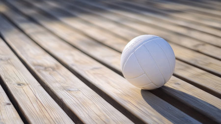 A focused shot of a volleyball on wooden flooring, beautifully illuminated by natural light, showcasing the simplicity and elegance of the sport equipment.の素材