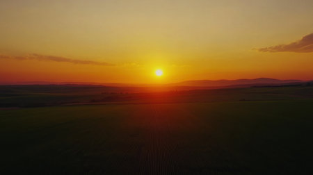A breathtaking view of a sunset illuminating the horizon over rolling hills and fields, capturing the serene beauty of nature in vibrant, warm colors.の素材