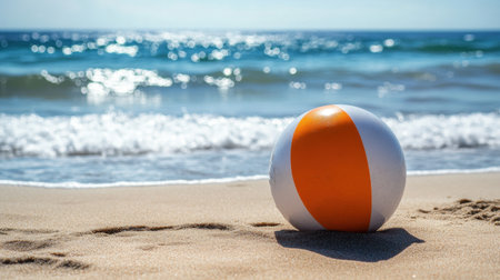 A vibrant beach ball rests on a golden sandy shore, with gentle waves lapping at the beach, creating a serene atmosphere perfect for summer enjoyment and relaxation by the ocean.の素材