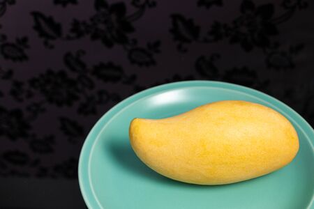 The yellow ripe mango in a glossy green tile palette reflects walls with floral patterns.の写真素材