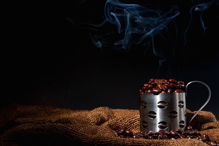 Freshly roasted coffee, put in a stainless steel cup Brown sack flooring Black background Dark imageの写真素材