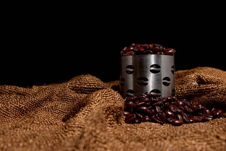 Freshly roasted coffee, put in a stainless steel cup Brown sack flooring Black background Dark imageの写真素材