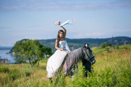 Beautiful and stunning bride,  on a horse in the nature, on her wedding dayの写真素材