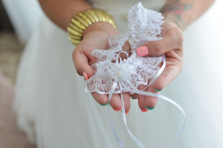 Garter on the leg of a bride, slim sexy bride in wedding luxury dress showing her silk garter with golden ribbon. woman have a final preparation for wedding ceremony. Wedding day momentsの写真素材