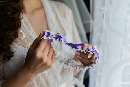 Garter on the leg of a bride, slim sexy bride in wedding luxury dress showing her silk garter with golden ribbon. woman have a final preparation for wedding ceremony. Wedding day momentsの写真素材