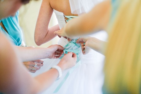 Garter on the leg of a bride, slim sexy bride in wedding luxury dress showing her silk garter with golden ribbon. woman have a final preparation for wedding ceremony. Wedding day momentsの写真素材